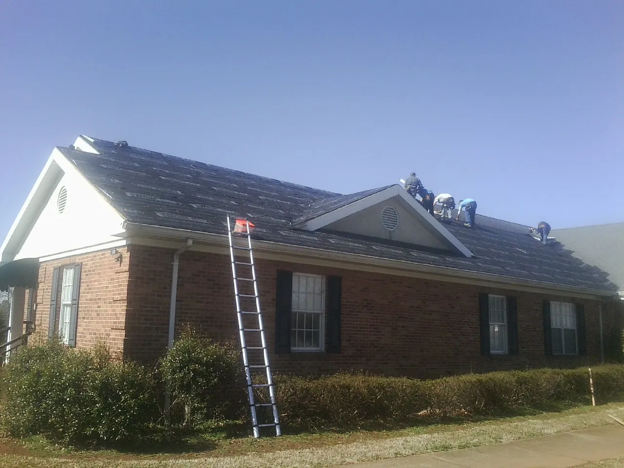 Crew tearing shingles off a brick ranch roof with a ladder set — Emergency Roof Repair work by our crew in Johnsonville