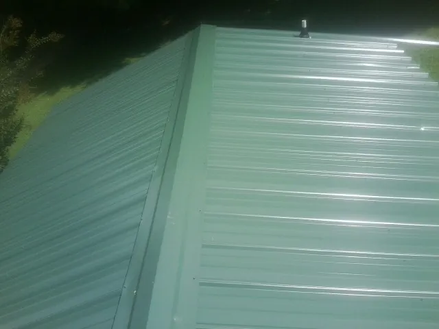 New green metal panels meeting at the ridge of a roof — Flat Roof Repair work by our crew in Johnsonville