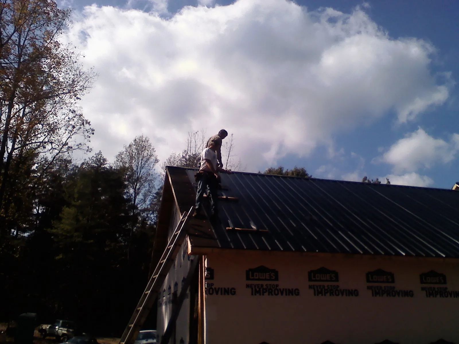 Roofer fastening dark metal panels high against a cloudy sky, from a Roof Inspection job in Johnsonville