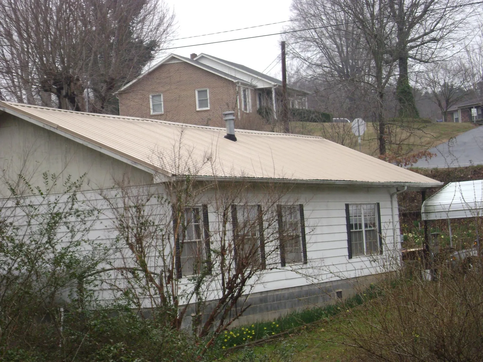 Tan metal roof on a white sided house set into a hillside — Commercial Roofing by Roofing Brothers in Johnsonville